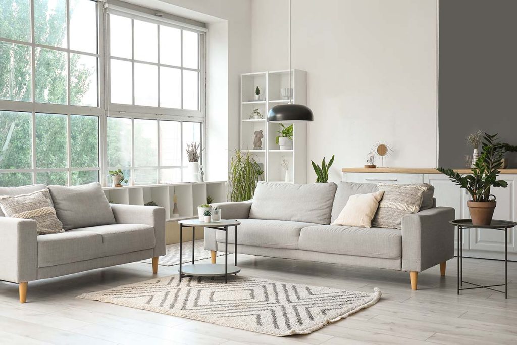 Interior of light living room with cozy grey sofas, coffee table and big window